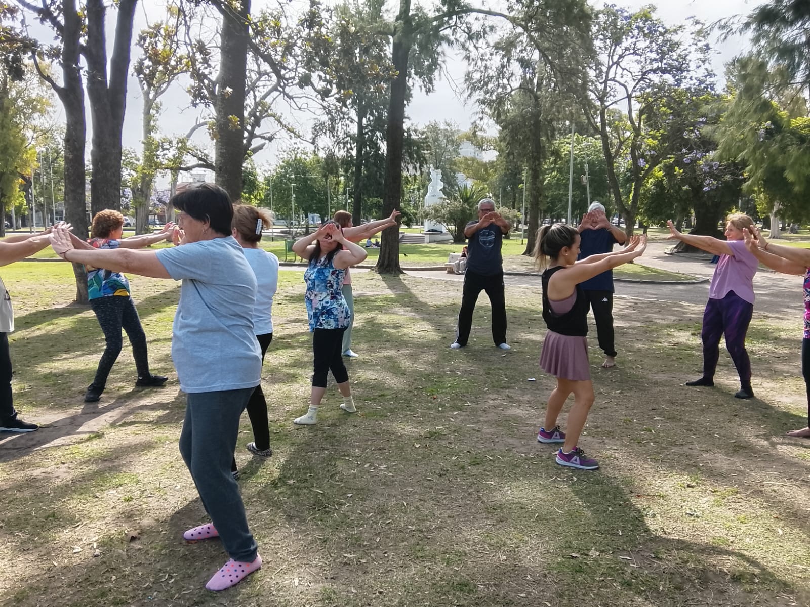 Grupo practicando Tai Chi al aire libre con los brazos extendidos en una plaza de Zona Sur